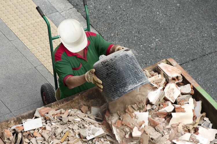 Man in a hard hat disposing waste into skip